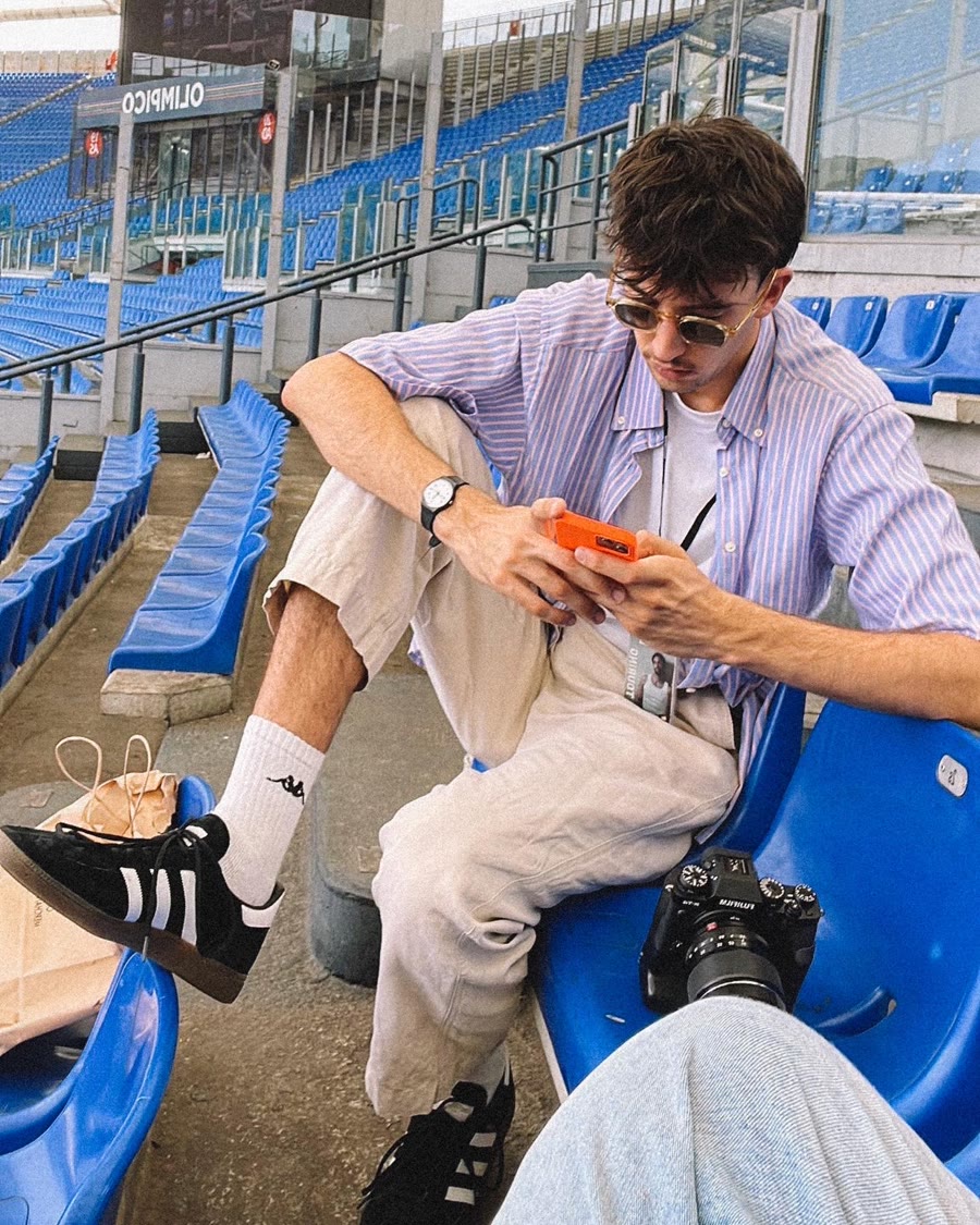 Nic seduto sugli spalti di uno stadio, con il telefono in mano e la macchina fotografica accanto